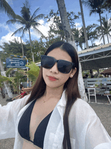 a woman wearing sunglasses stands in front of a blue sign that says ' emblema beach ' on it