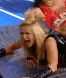 two women are wrestling in a ring and one of them is laying on the ground .