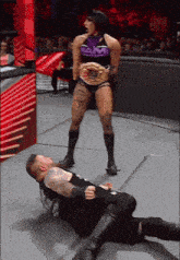 a woman in a purple top with the word ram on it is standing over a wrestler