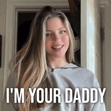 a woman with long blonde hair is wearing a grey shirt that says " i 'm your daddy " on it
