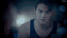 a man in a black tank top is standing in a dark room .