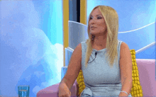 a woman is sitting on a couch with a glass of water and a microphone .