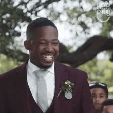 a man in a maroon suit and tie smiles while walking down the aisle at a wedding