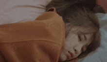 a woman is wrapped in an orange blanket and sleeping