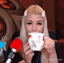 a woman is drinking from a mug with a cat on it in front of two microphones .