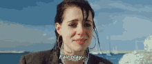 a woman is crying and saying `` fair play '' while standing in front of a body of water .