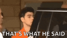 a man in an orange shirt is standing next to a car with the words `` that 's what he said '' written on it .