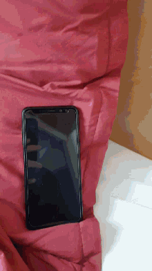 a cell phone is laying on a bed with a red blanket