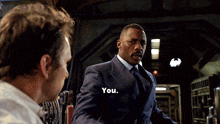 a man in a suit and tie is talking to another man in a white shirt and says you