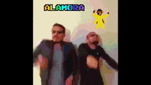 two men are dancing in front of a wall that says alamora on it