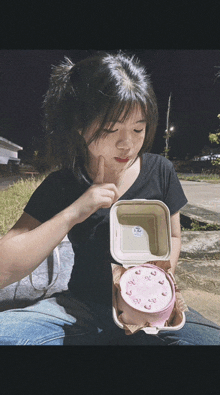 a girl in a black shirt is holding a pink cake in a styrofoam box