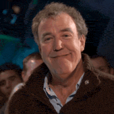 a man wearing a brown sweater and a blue shirt is smiling