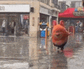 a stuffed animal is walking down a wet street in front of a store .
