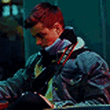 a man wearing a denim jacket and a purple scarf is sitting in a dark room .