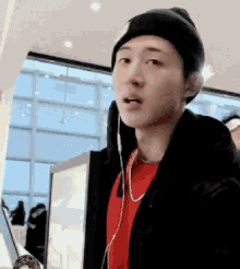 a man wearing headphones and a beanie is standing in front of a computer screen .