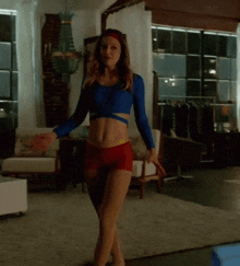 a woman in a blue crop top and red shorts is standing in a living room .