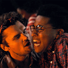 a man wearing glasses talks to another man in a red shirt