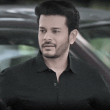 a man with a beard wearing a black shirt is standing in front of a vehicle