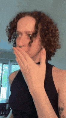 a woman with curly hair covers her mouth with her hand