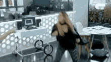 a woman is dancing in a room with a table and chairs in front of a computer .