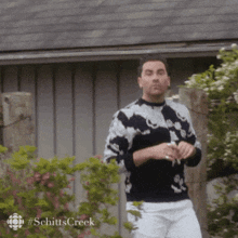 a man in a black and white tie dye sweater stands in front of a building