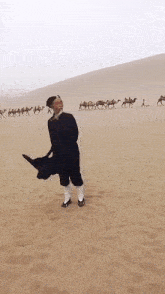 a man is standing in the middle of a desert with a caravan of camels behind him .