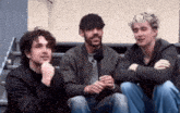 three men are sitting on a set of stairs and one of them is holding a microphone .