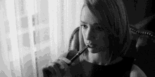 a black and white photo of a woman sitting in a chair holding a pen in her mouth .
