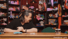 a man sits at a table with a mug that says ' meldivar arts ' on it