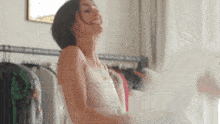 a woman in a white tank top is dancing in a room with clothes hanging on a rack .