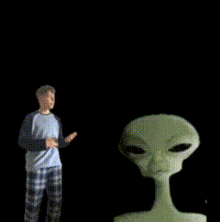 a man in plaid pajamas stands in front of a grey alien