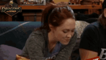 a woman sitting on a couch with a dragon 's nothings logo in the background