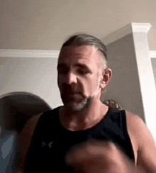 a man with a beard wearing a black tank top is standing in a living room .