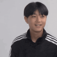 a young man wearing a black jacket with white stripes on the sleeves is smiling .