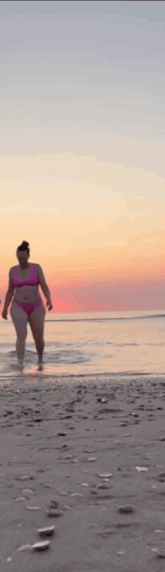 a woman in a pink bikini is walking along the beach at sunset .