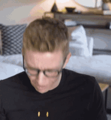 a man wearing glasses and a black shirt has a yellow smiley face on his shirt