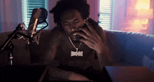 a shirtless man is sitting on a couch talking on a cell phone while wearing a necklace that says king kong