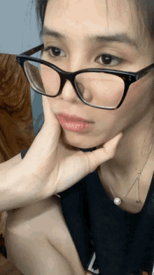 a woman wearing glasses holds her hand to her face