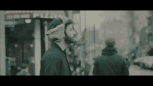 a man wearing a fur hat is walking down a street in front of a pizza shop
