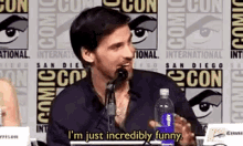 a man speaking into a microphone with the words i 'm just incredibly funny below him