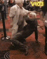 a man in a white suit is kneeling down next to another man in a black suit with the number 103 on the bottom