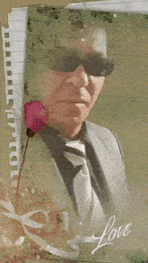 a man in a suit and tie is holding a pink rose in front of a piece of paper with the word love on it