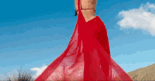 a woman in a red dress is standing in front of a blue sky with clouds
