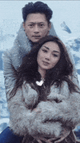 a man and a woman are posing for a picture in front of a snowy mountain