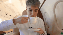a man in a white shirt drinking from a white cup