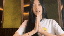 a girl with long black hair is wearing a white t-shirt with a banana on it and is praying with her hands together .