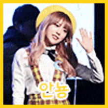 a girl wearing a yellow hat and a plaid dress is waving at the camera .