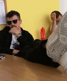 a man wearing sunglasses sits at a table with his feet up and a red bottle that says o'neill
