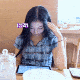 a girl in a plaid shirt is sitting at a table with a tablet in front of her
