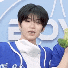 a young man in a blue jacket is holding a stuffed frog in his hands .